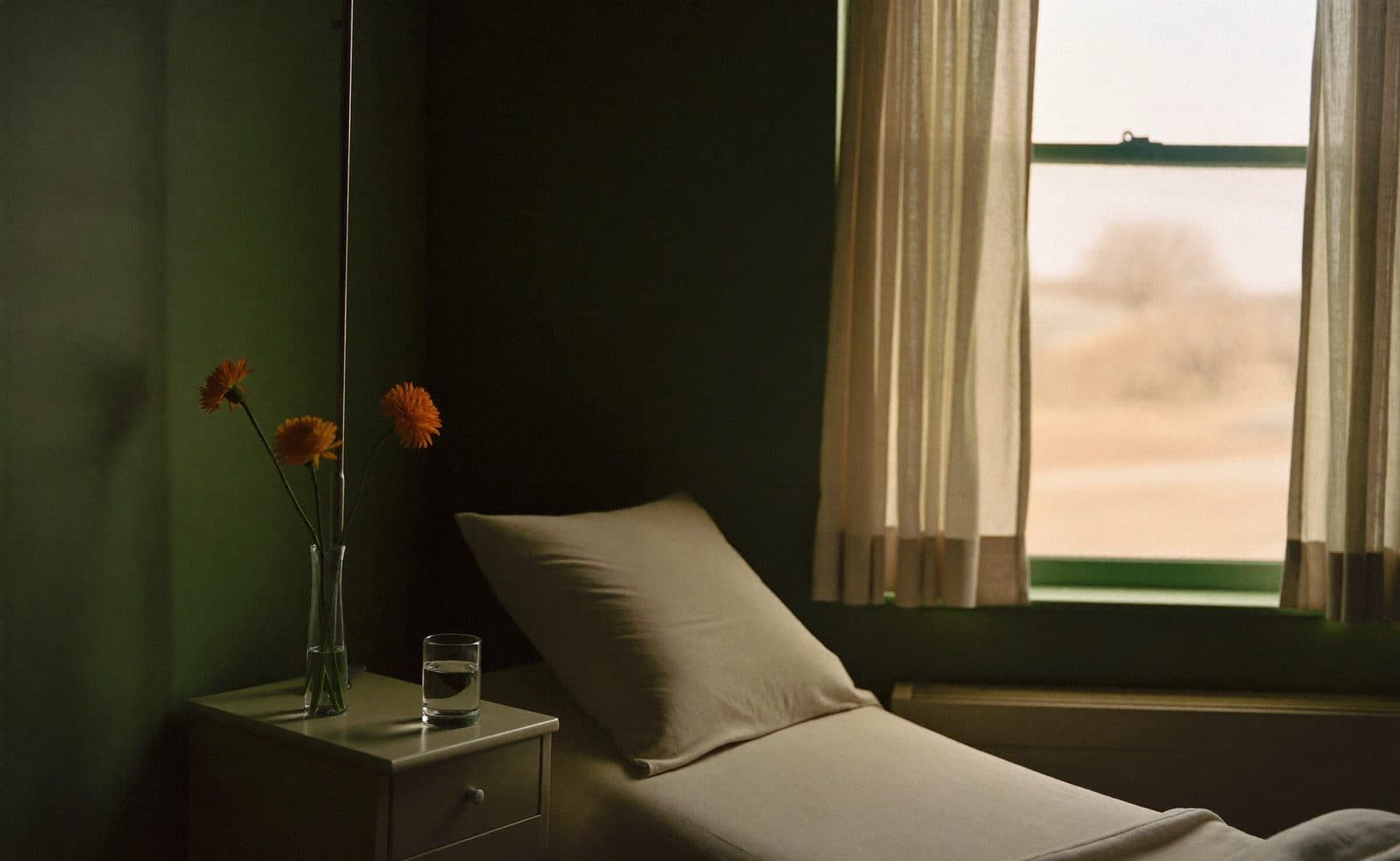A quiet private recovery room with a neatly made bed, a glass of water and marigolds on the bedside table