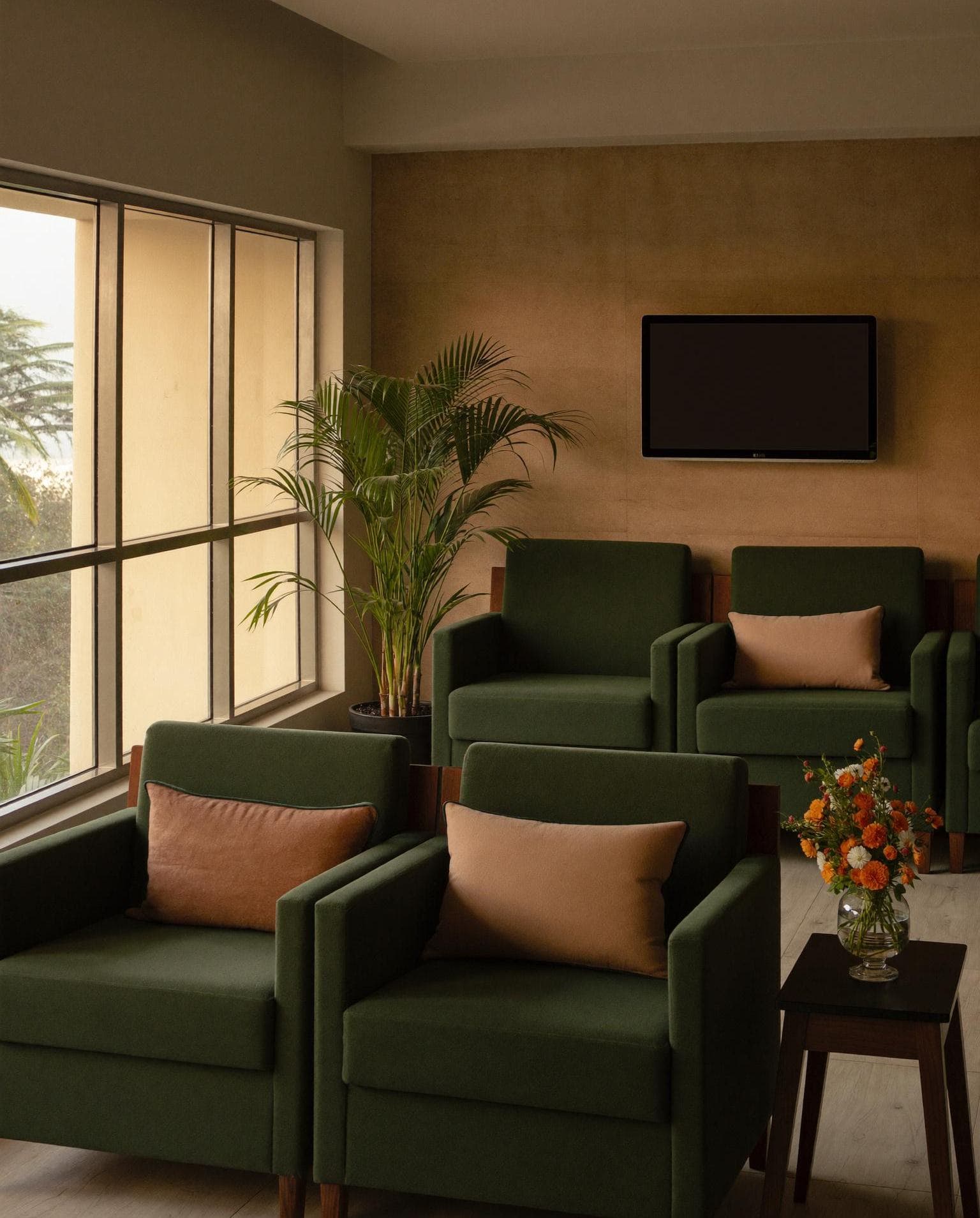 A calm, warm hospital waiting lounge in India with green armchairs and marigold flowers